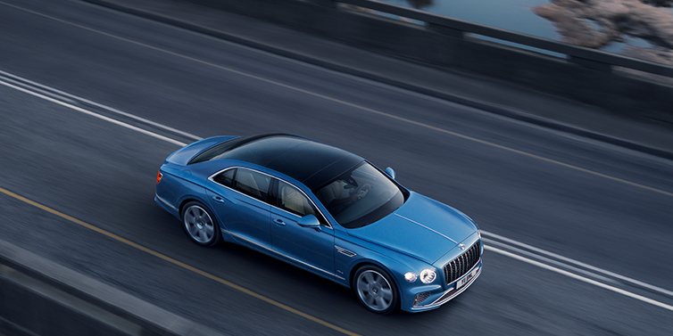 Bentley Tel Aviv New Bentley Flying Spur Azure sedan in Light windsor blue paint by Mulliner, with 22 inch Azure wheels seen from overhead driving dynamically on a country road