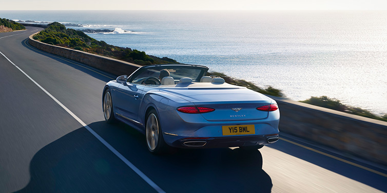 Bentley Tel Aviv New Bentley Continental GTC Azure convertible rear view in Light Windsor blue paint with 22 inch ten spoke wheels driving dynamically on an ocean road in the sunshine