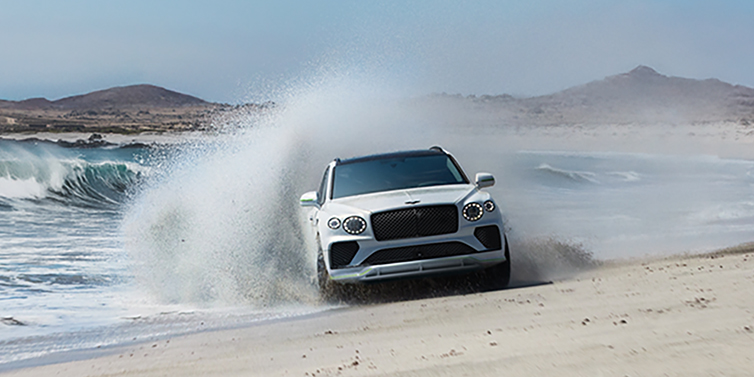 Bentley Tel Aviv Bentley Bentayga Speed SUV facing front in Snow Quarts Pearlescent white paint driving dynamically on beach