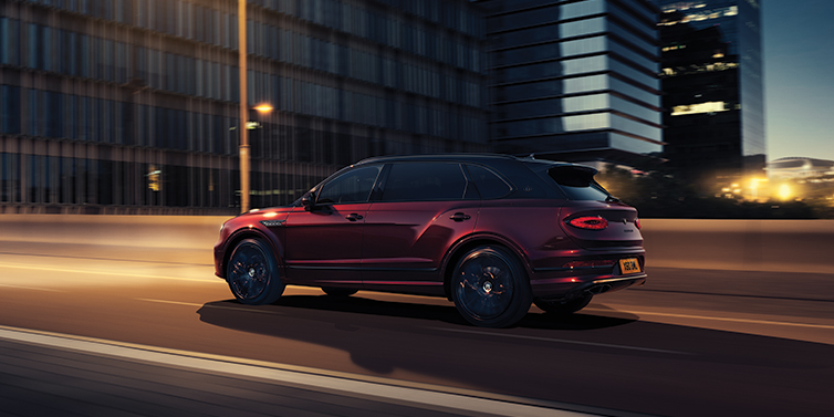 Bentley Tel Aviv Bentley Bentayga Extended Wheelbase Mulliner SUV in Cricket Ball red paint driving dynamically in city at night
