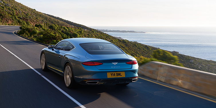 Bentley Tel Aviv New Bentley Continental GT Azure coupe in Light Windsor blue paint seen from the rear driving dynamically on a seaside road