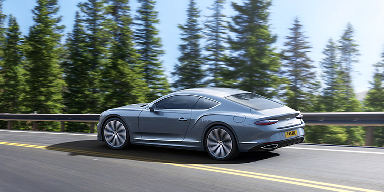Bentley Tel Aviv New Bentley Continental GT coupe in Silverlake paint, seen from the rear, driving dynamically on a tree-lined road